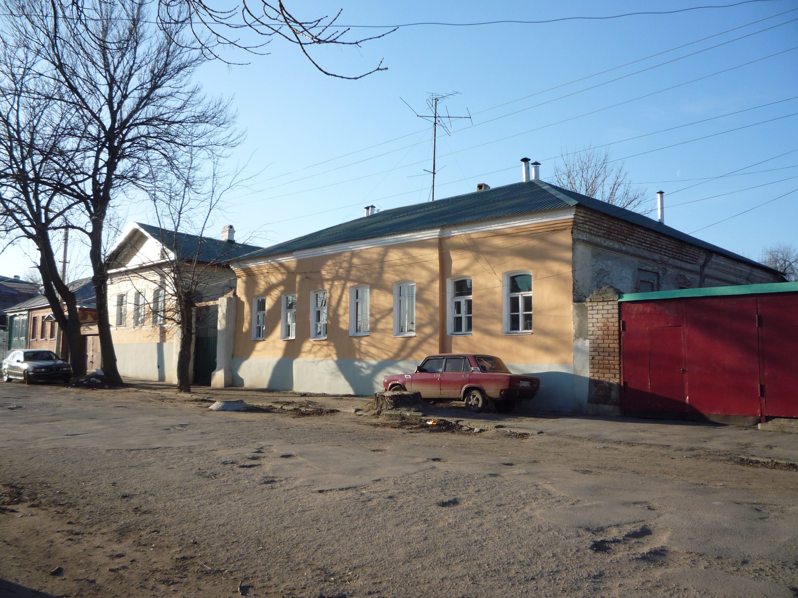 Одноэтажный дом усадьбы на Октябрьской, 163 справа и флигель с фронтоном слева, между ними ворота.