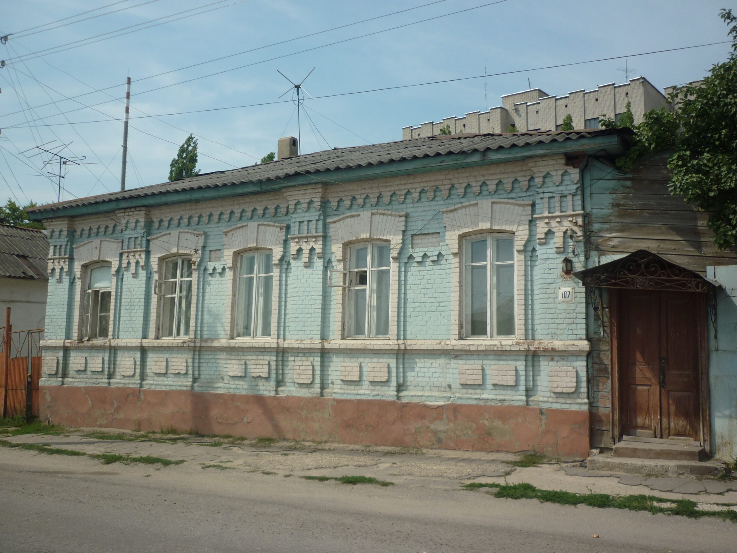 Одноэтажный дом на Советской, 107 с кирпичной облицовкой, высокими окнами и входом справа.
